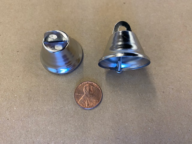 Two small metallic bells (blue-tinted) placed on a brown surface, with a penny for scale showing a Lincoln portrait in the center of the image.