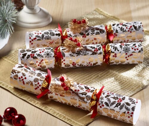Wrapped Christmas presents on a wooden table with white-and-gold patterned paper, red ribbons, and gold pine sprigs on a gold runner.